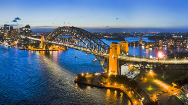 Dark Sydney city CBD landmarks around Sydney Harbour connected by Sydney Harbour bridge and bright cahill expressway illuminated and reflecting in water.