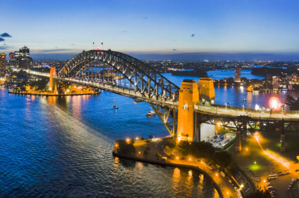 Dark Sydney city CBD landmarks around Sydney Harbour connected by Sydney Harbour bridge and bright cahill expressway illuminated and reflecting in water.